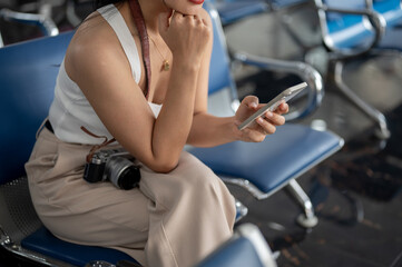 A female traveler using her smartphone while sitting at a waiting seat in the airport terminal.
