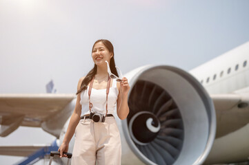 A confident Asian female tourist is carrying her luggage and walking on the runway on a sunny day.
