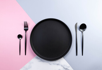 Top view of black plate and cutlery on colourful background. Table setting, blue, pink and marble...