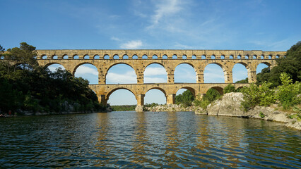 Pont du Gard famous aqueduct arched bridge mirroring in Gardon river, popular tourist landmark in...