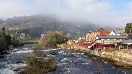 Looking up the river Dee at llangollen. In the distance the low cloud is covering the hills. The train station is to the right with carriages visible.