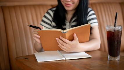 A young Asian woman is reading a book or doing homework in a beautiful vintage coffee shop.