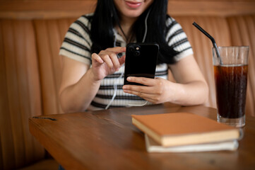 A woman sitting in a coffee shop, using her phone and listening to music on her headphones.