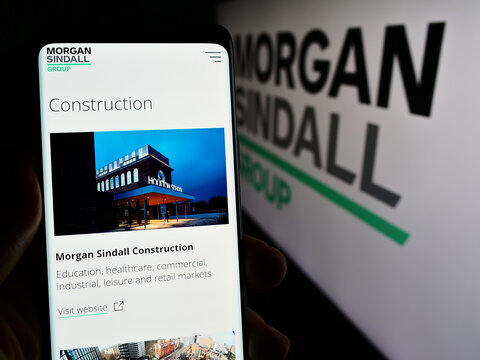 Stuttgart, Germany - 03-25-2024: Person holding mobile phone with web page of British construction company Morgan Sindall Group plc with logo. Focus on center of phone display.