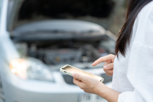 breakdown, broken car, repair. Woman uses mobile phone check insurance premiums through application due to car accident . Find garage to get car fixed during country tour, waiting for help, emergency.