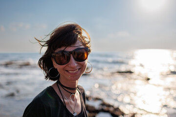 portrait of a stylish girl in sunglasses with hair fluttering in the wind by the sea. - 776950447