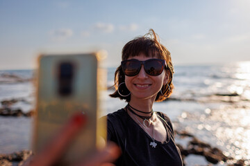 girl in sunglasses with hair flying in the wind, taking a selfie by the sea. - 776950807