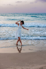 Fototapeta na wymiar happy young girl in a white summer dress walks along the beach at sunset.