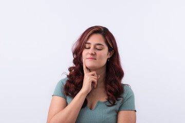 Fototapeta premium Horizontal portrait of a pensive young woman with her hand resting on her face with reflective gesture looking down. Light background and copy space. Promotion and marketing concept