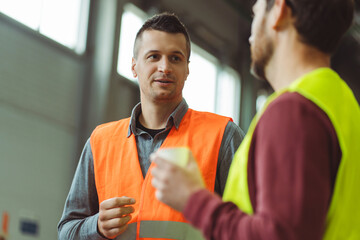 Successful, professional foreman, worker, engineer talking to employee while standing in warehouse