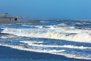 Fototapeta na wymiar Waves in the rough North sea with some people walking along the shore