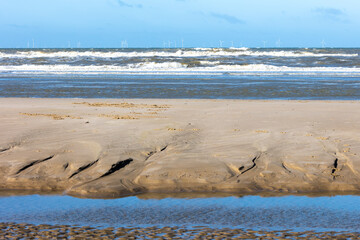 Structures in the sand on a beach of the North sea, with a rough sea with spindrift waves in the background