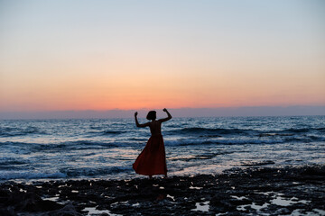 beautiful sensual woman in a red long dress posing on the seashore during sunset. beautiful sunset. - 776958041