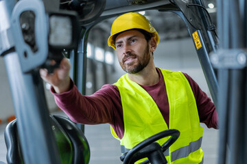 Smiling bearded man driver professional worker wearing hard hat and workwear driving forklift