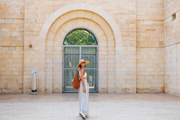 A stylish fashionable girl traveler in a brown hat with a backpack stands in front of an old house while traveling. visiting a museum while traveling. - 776959676