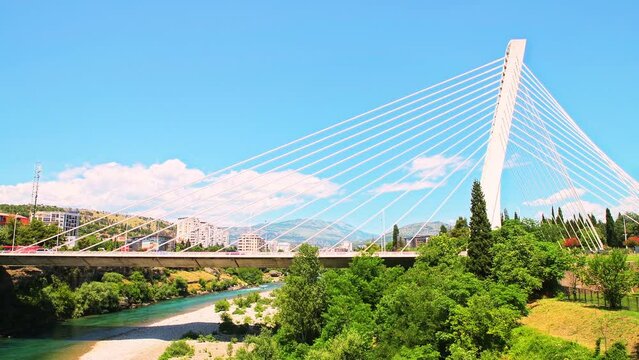 Millennium bridge over Moraca river by Podgorica, Montenegro cityscape with view on mountains and trees in the park in summer