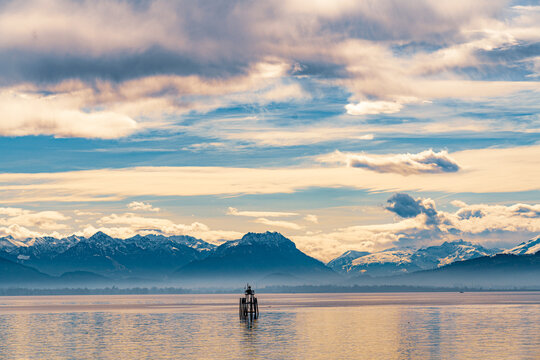 Bodensee in Abendstimmung mit Wolken &uuml;ber der Seefl&auml;che; das Seezeichen L&auml;utwerk vor der Lindauer Hafeneinfahrt un die Alpengipfel von R&auml;tikon und Glarner Alpen