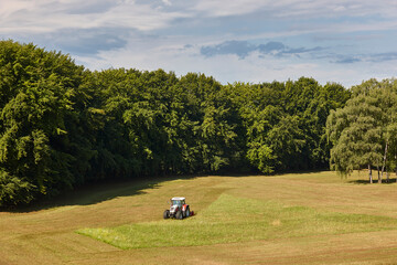 Tractor mowing grass. Meadow sorrounded by forest. Agriculture industry