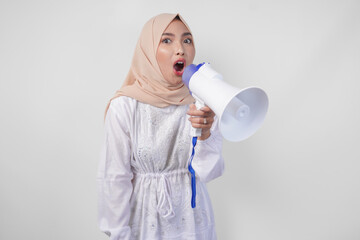 Overjoyed Asian woman wearing hijab and white dress shouting to the megaphone making announcement,...