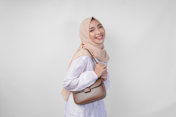 Stylish young Asian Muslim woman wearing white dress and hijab with brown sling bag smiling happily...