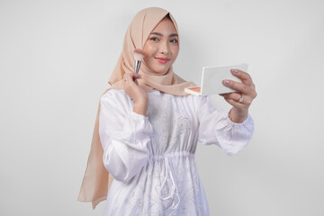 Beautiful young Asian Muslim woman wearing white dress and hijab applying make up using brush. Fashion and cosmetics beauty concept