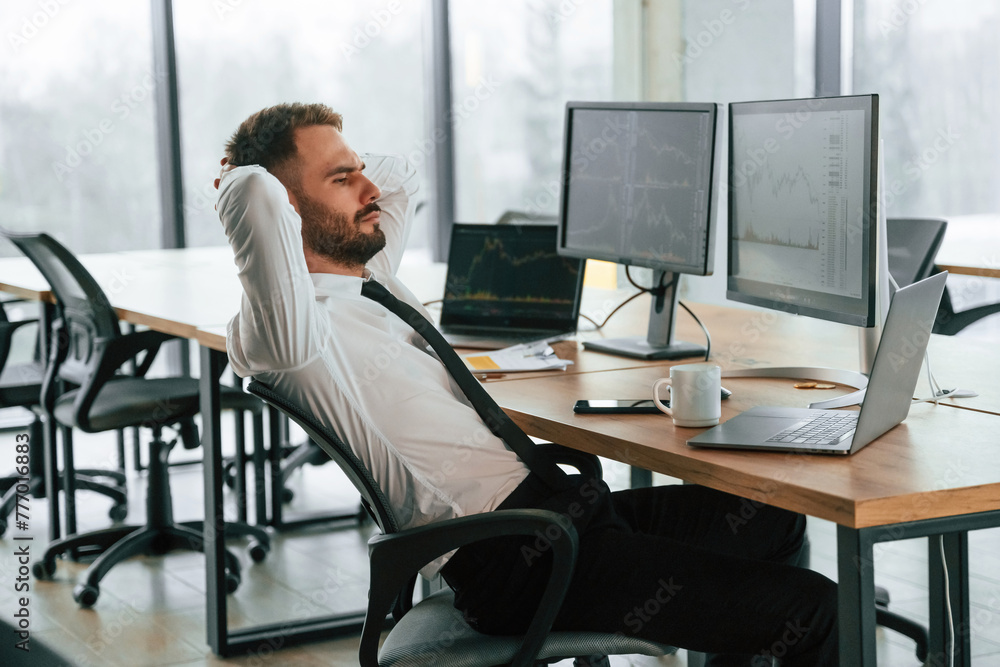 Poster sitting with hands behind the head. businessman is by computer and working in the office