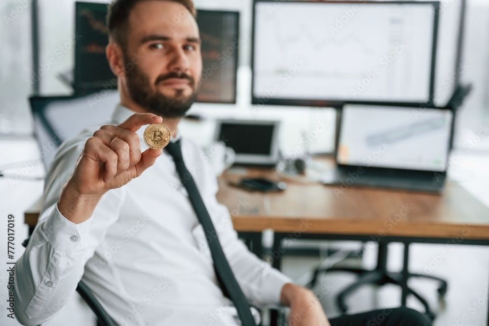 Poster showing golden coin that is in hand. businessman is sitting by computer and working in the office
