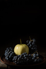 Blue grapes and green apple on a clay plate