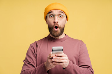 Portrait of surprised attractive man in glasses holding mobile phone isolated