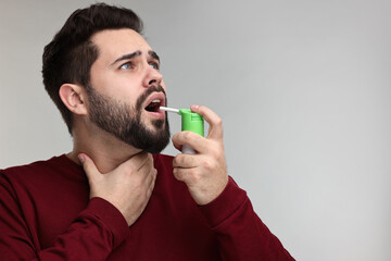 Young man using throat spray on grey background. Space for text - obrazy, fototapety, plakaty