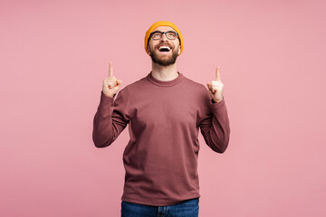 Amazed middle aged bearded man 40s, in eyeglasses and yellow hat pointing his index fingers up