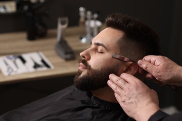 Professional barber shaving client's beard with blade in barbershop, closeup