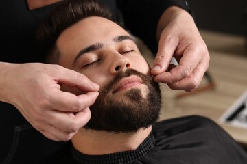 Obraz premium Professional barber working with client's mustache in barbershop, closeup
