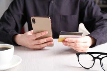 Online payment. Woman with smartphone and credit card at white wooden table, closeup