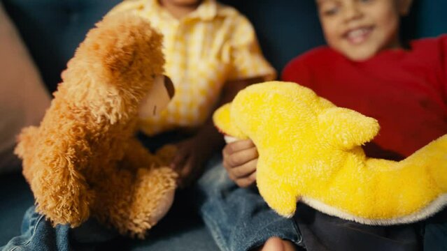 Two happy kids playing with plush toys on sofa, holding teddy bear and dolphin