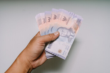 A wad of 10,000 rupiah bills, still sealed with the bank logo, was placed on a white mat. This...