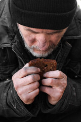 Poor homeless man holding piece of bread outdoors