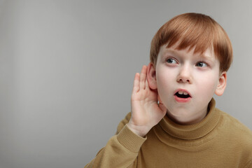 Little boy with hearing problem on grey background, space for text