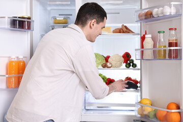 Happy man taking eggplant out of refrigerator in kitchen