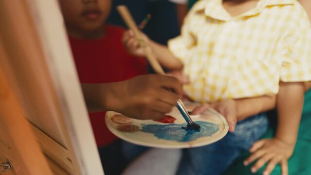 African American boys mixing acrylic paints with a brush, painting on a canvas