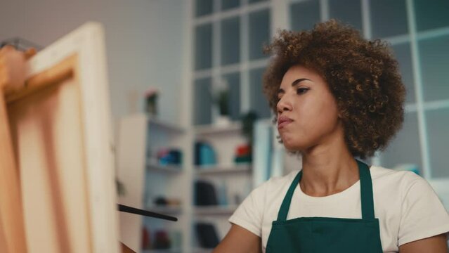 Woman painter trying to paint at an easel stand, displeased with results