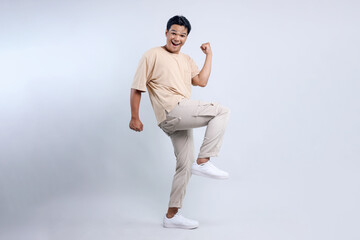 Full length view of cheerful Asian man clenched fist and dancing rejoicing victory isolated on white background