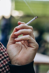 A man's hand holds a thin smoking cigarette