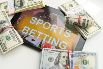 tablet pc with app for sport bets, on top of stacks of banknotes, white background, concept of...