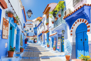 Photograph of the blue stairs in Chefchaouen, Morocco with pots on it, colorful houses and plants on a sunny day