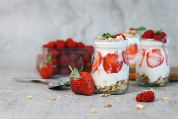 Three glasses of strawberry parfaits with yogurt and granola on grey background