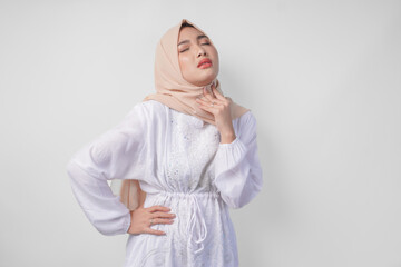 Tired Asian Muslim woman in white dress and hijab holding her neck feeling thirsty waiting for...