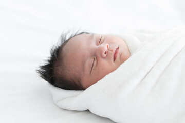 Adorable newborn baby wrapped in white swaddle towel lying on bed and sleeping peacefully. Sleeping infant in a wrap on white blanket. Beautiful close up portrait of little child girl 19 days