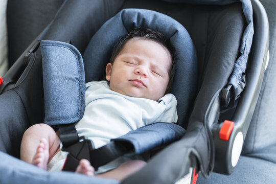 Portrait of adorable less than one month old newborn baby girl sleeping in the modern car seat with fastening safety belt. Selective focus on little Asian Australian child