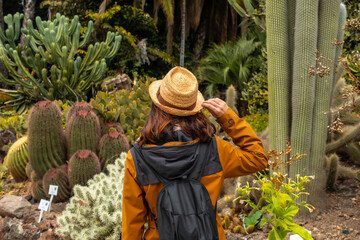 A woman wearing a straw hat walks through a desert garden